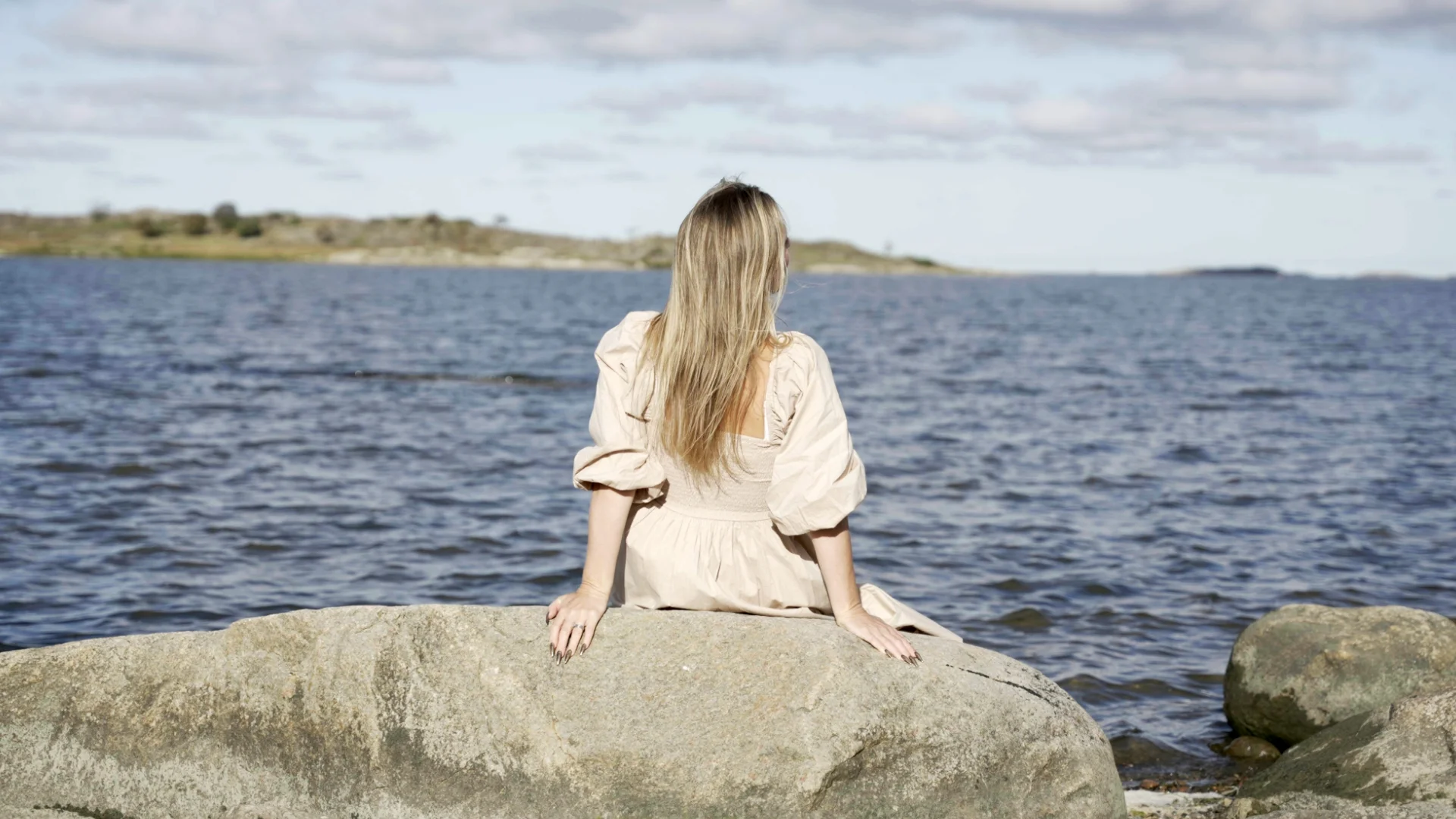 Kvinna sitter på en sten vid havet